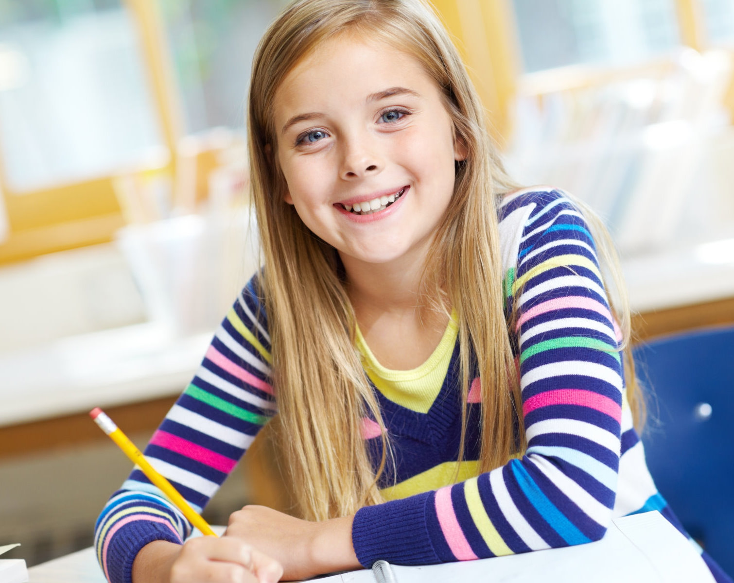 Happy girl smiling at you while writing in her notebook at school - copyspace