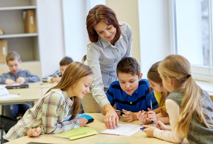 education, elementary school, learning and people concept - teacher helping school kids writing test in classroom