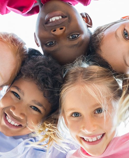 Closeup face of happy multiethnic children embracing each other and smiling at camera. Team of smiling kids embracing together in a circle. Portrait of young boy and pretty girls looking at camera.